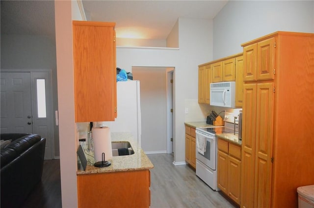 kitchen featuring light wood-type flooring, white appliances, and light stone counters