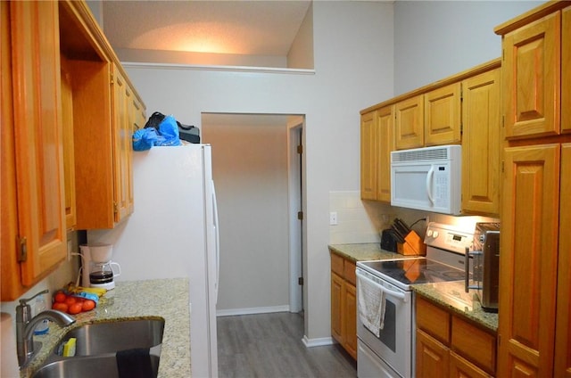 kitchen featuring light stone counters, brown cabinets, a sink, wood finished floors, and white appliances