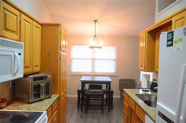 kitchen with a textured ceiling, white appliances, dark wood-style flooring, a sink, and decorative light fixtures