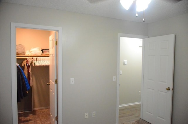 bedroom with a textured ceiling, a ceiling fan, baseboards, a closet, and a walk in closet