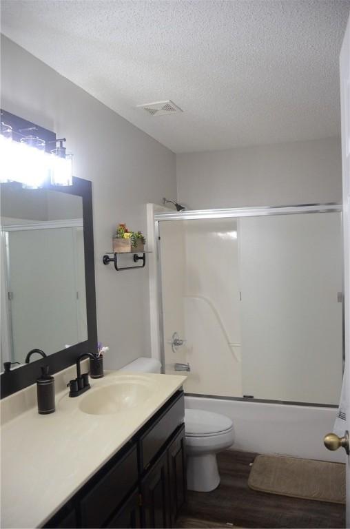 bathroom featuring toilet, wood finished floors, vanity, visible vents, and combined bath / shower with glass door