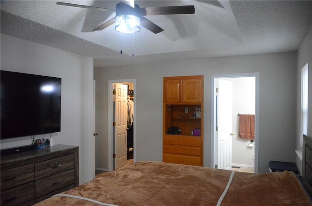 bedroom featuring ceiling fan, a textured ceiling, ensuite bath, and a spacious closet