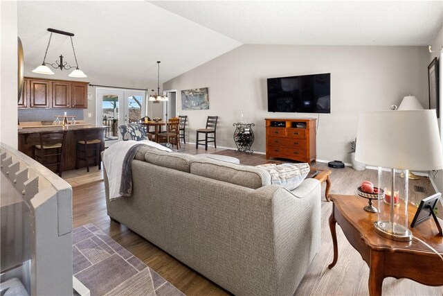 living area featuring baseboards, light wood finished floors, a chandelier, and vaulted ceiling