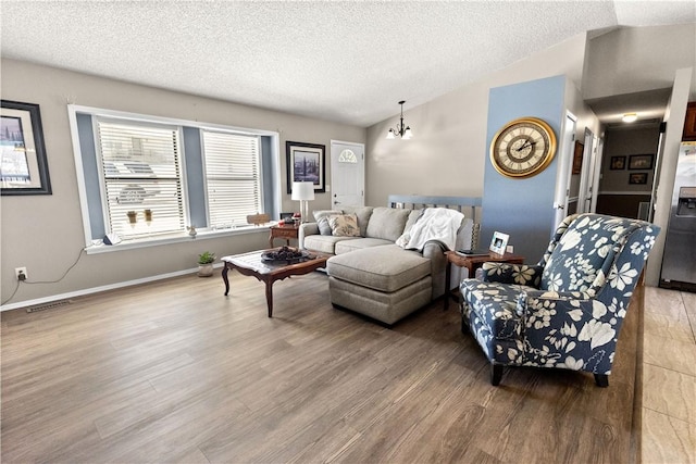 living room with a textured ceiling, a chandelier, baseboards, wood finished floors, and vaulted ceiling