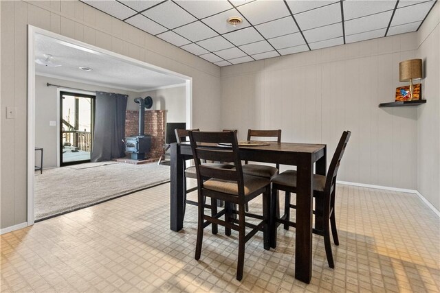 dining space featuring visible vents, baseboards, light floors, a wood stove, and a paneled ceiling