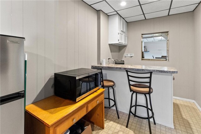 kitchen featuring a kitchen bar, light countertops, white cabinets, freestanding refrigerator, and a peninsula