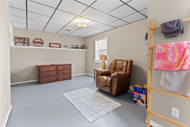 living area featuring baseboards, a paneled ceiling, and finished concrete flooring