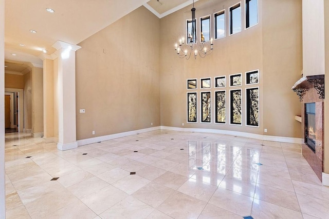 interior space with a notable chandelier, a towering ceiling, baseboards, ornamental molding, and a glass covered fireplace