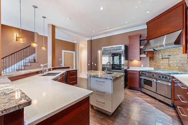 kitchen with premium appliances, decorative light fixtures, wall chimney range hood, light stone countertops, and a center island with sink