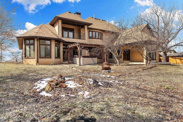 rear view of property with a balcony, a fire pit, stucco siding, a pergola, and a hot tub