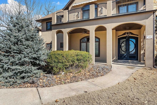 view of exterior entry featuring a balcony, ceiling fan, and stucco siding