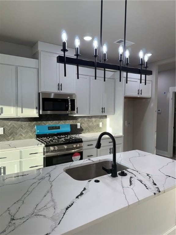 kitchen featuring white cabinets, decorative light fixtures, light stone countertops, stainless steel appliances, and a sink