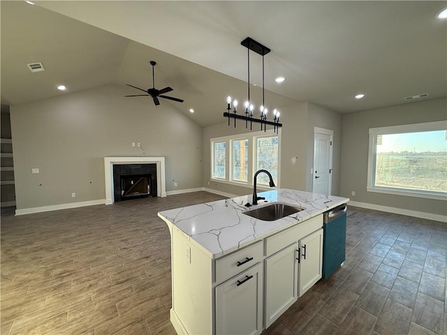 kitchen featuring stainless steel dishwasher, open floor plan, white cabinetry, a sink, and an island with sink