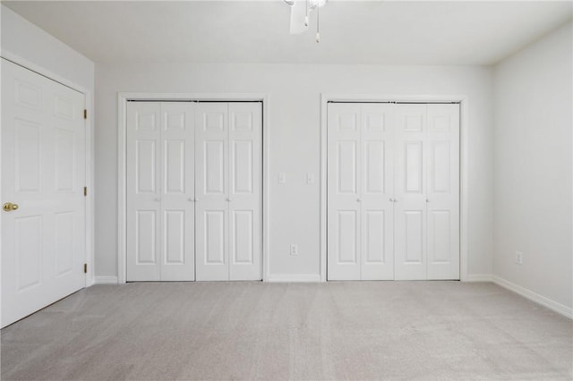 unfurnished bedroom with a ceiling fan, light colored carpet, baseboards, and two closets