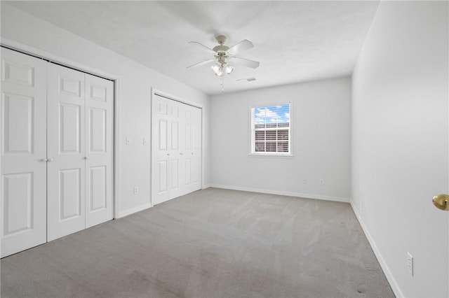 unfurnished bedroom with light carpet, ceiling fan, baseboards, and two closets