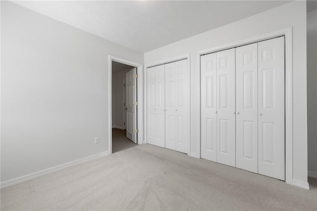 unfurnished bedroom featuring multiple closets, light colored carpet, and baseboards