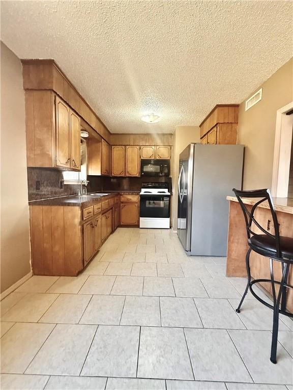 kitchen with white range with electric stovetop, brown cabinets, dark countertops, freestanding refrigerator, and black microwave