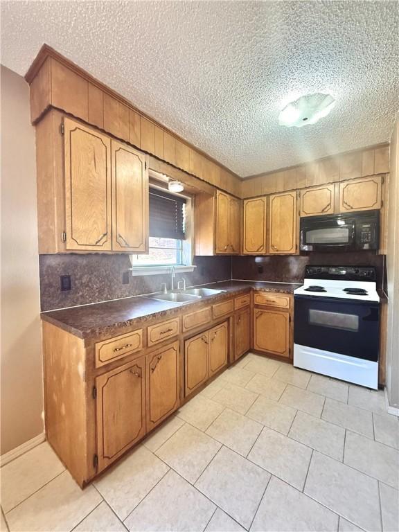 kitchen featuring black microwave, a sink, electric stove, brown cabinets, and dark countertops