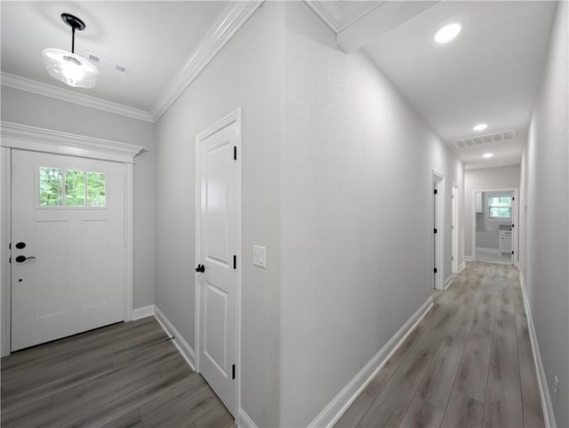 corridor featuring ornamental molding, visible vents, baseboards, and wood finished floors