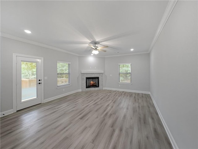 unfurnished living room with crown molding, a lit fireplace, a wealth of natural light, and baseboards