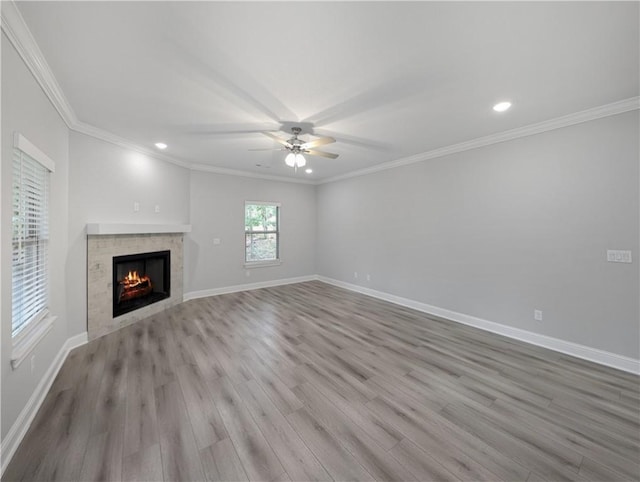 unfurnished living room featuring a tiled fireplace, ornamental molding, ceiling fan, light wood-type flooring, and baseboards