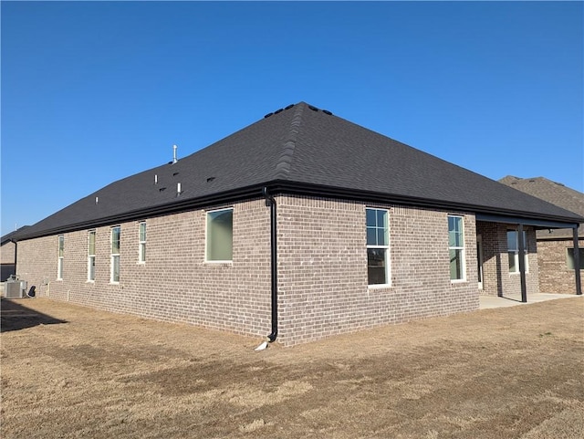 rear view of property featuring brick siding, a yard, central AC, and a patio