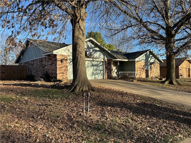 view of front of property featuring a garage, brick siding, driveway, and fence