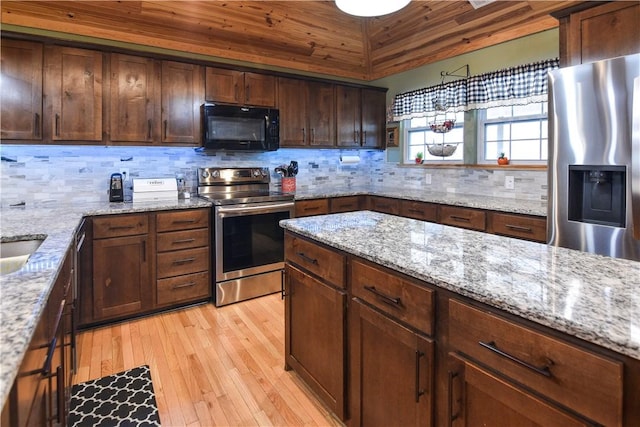 kitchen with lofted ceiling, light stone counters, appliances with stainless steel finishes, light wood-type flooring, and backsplash