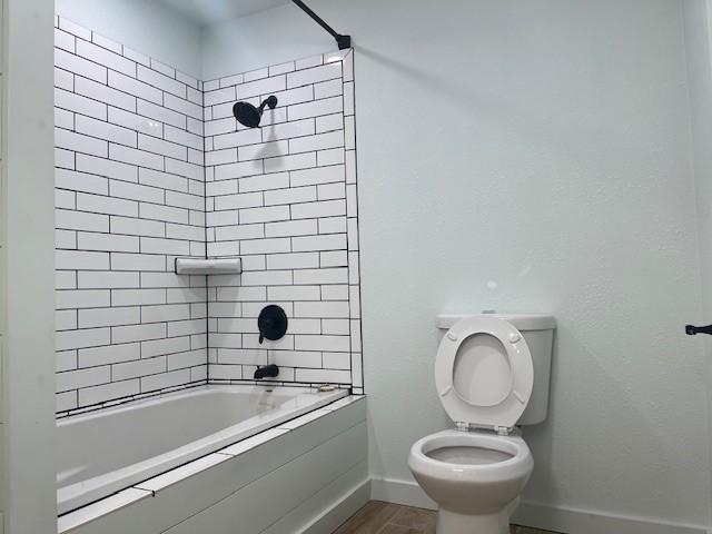 full bathroom featuring baseboards, tiled shower / bath, toilet, and wood finished floors