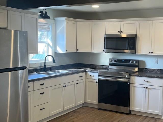 kitchen with dark wood-style floors, appliances with stainless steel finishes, white cabinets, and a sink