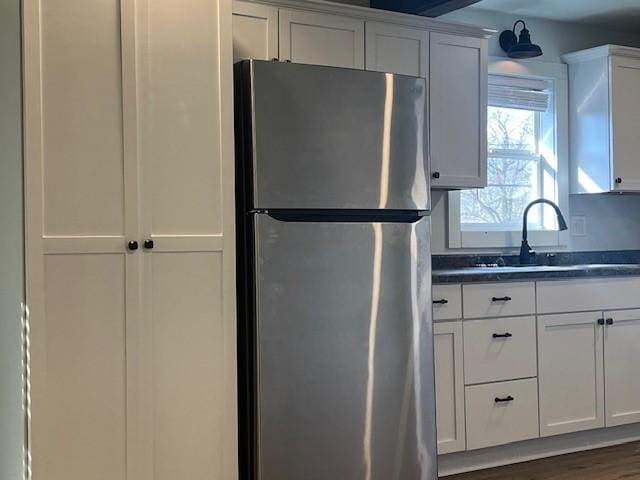 kitchen with dark countertops, white cabinets, a sink, and freestanding refrigerator