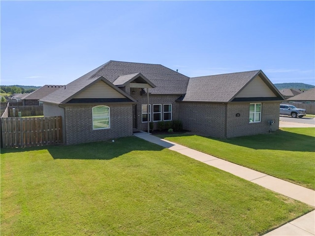 view of front facade with a shingled roof, brick siding, fence, and a front lawn