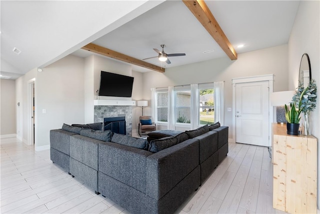 living room with ceiling fan, vaulted ceiling with beams, baseboards, light wood-style floors, and a glass covered fireplace