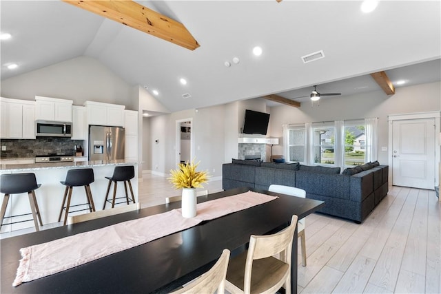 dining space featuring light wood finished floors, visible vents, a ceiling fan, beamed ceiling, and a fireplace