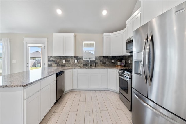 kitchen with decorative backsplash, appliances with stainless steel finishes, white cabinets, a sink, and a peninsula