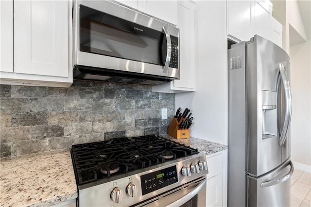 kitchen featuring stainless steel appliances, light stone counters, decorative backsplash, and white cabinets