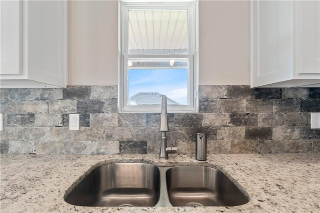 kitchen featuring light stone counters, decorative backsplash, a sink, and white cabinets