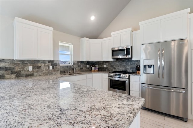 kitchen with light stone countertops, a sink, white cabinetry, appliances with stainless steel finishes, and decorative backsplash