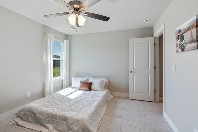 bedroom with light wood-style floors, ceiling fan, visible vents, and baseboards