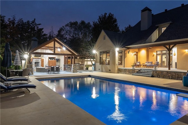 pool at night with an exterior structure, a patio area, area for grilling, an outdoor structure, and an outdoor pool