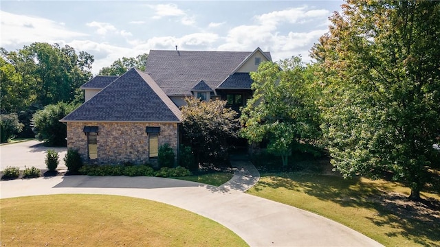 view of front facade featuring stone siding, a shingled roof, and a front yard