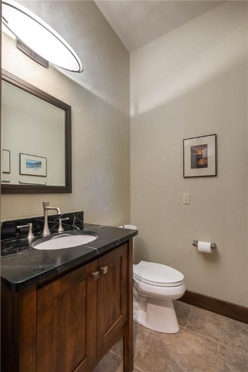 half bathroom featuring baseboards, vanity, and toilet