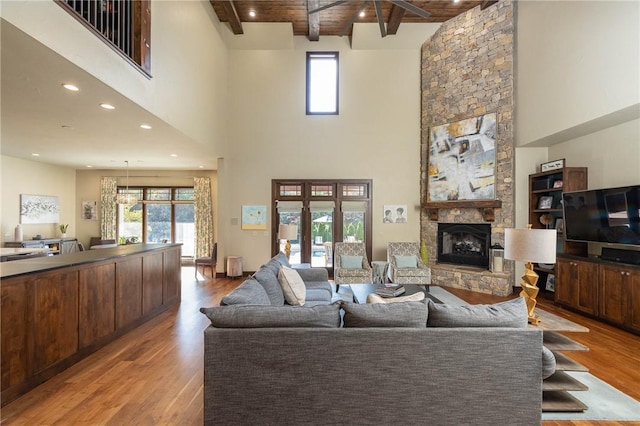 living room with a stone fireplace, a healthy amount of sunlight, beam ceiling, and light wood-style floors