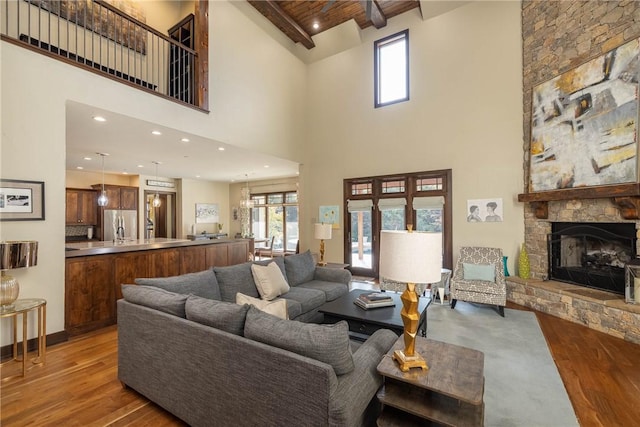 living area with wooden ceiling, a stone fireplace, beamed ceiling, and wood finished floors