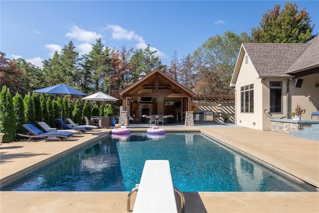 pool with an outbuilding, an outdoor fireplace, exterior bar, a diving board, and a patio area