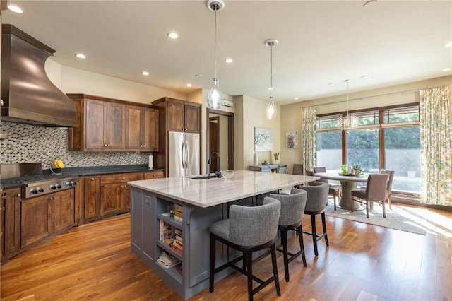 kitchen featuring island range hood, hanging light fixtures, appliances with stainless steel finishes, dark stone countertops, and a center island with sink