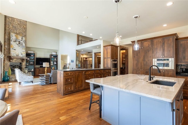 kitchen featuring light stone counters, a sink, open floor plan, hanging light fixtures, and an island with sink