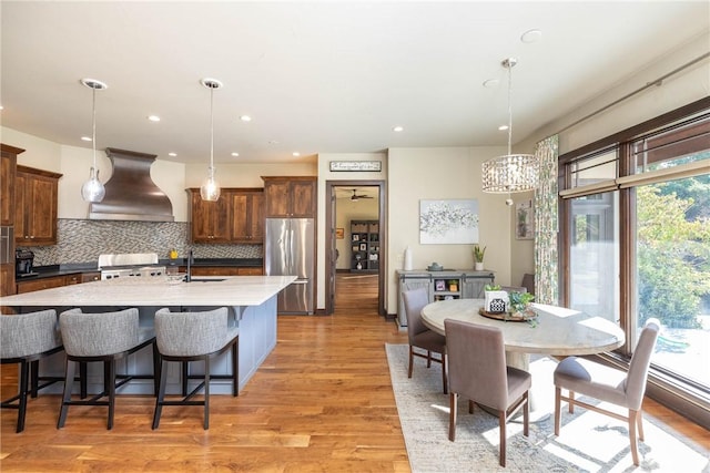 kitchen with freestanding refrigerator, premium range hood, hanging light fixtures, and a sink