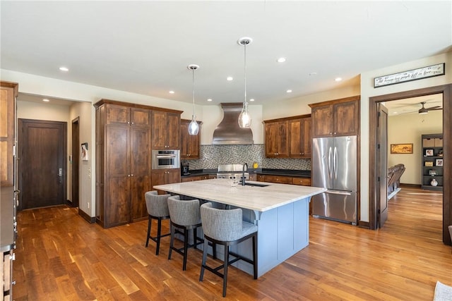 kitchen featuring range hood, dark wood finished floors, stainless steel appliances, a breakfast bar area, and backsplash