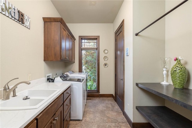 laundry room with washing machine and dryer, cabinet space, a sink, and baseboards